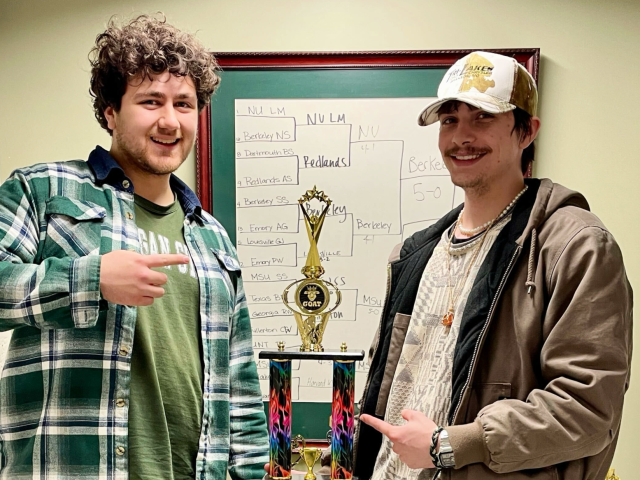 Tony Miklovis and Blaine Montford standing in front of trophies holding a large trophy