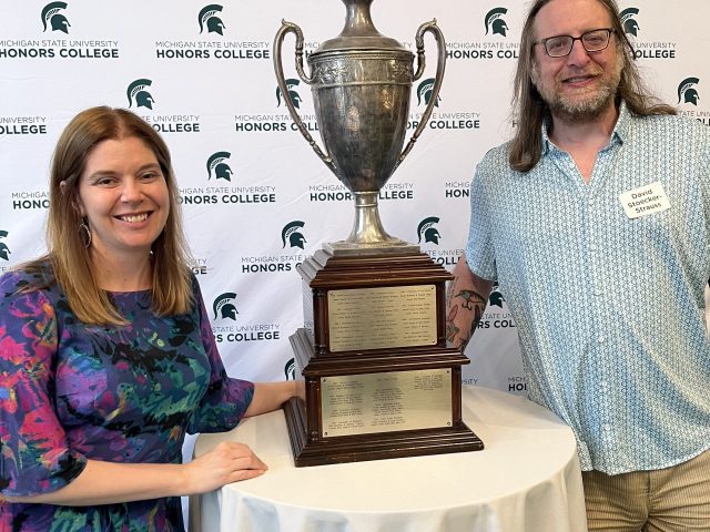 Greta Stahl and Dave Strauss with trophy in front of backdrop