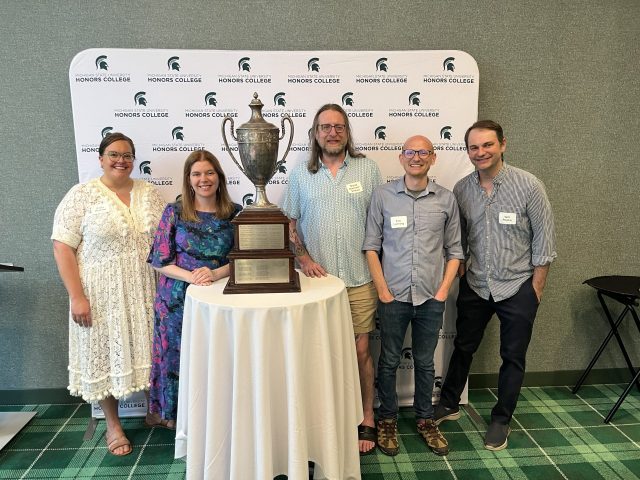 Carly Watson, Greta Stahl, David Strauss, Eric Lanning, and Will Repko standing with trophy in front of backdrop