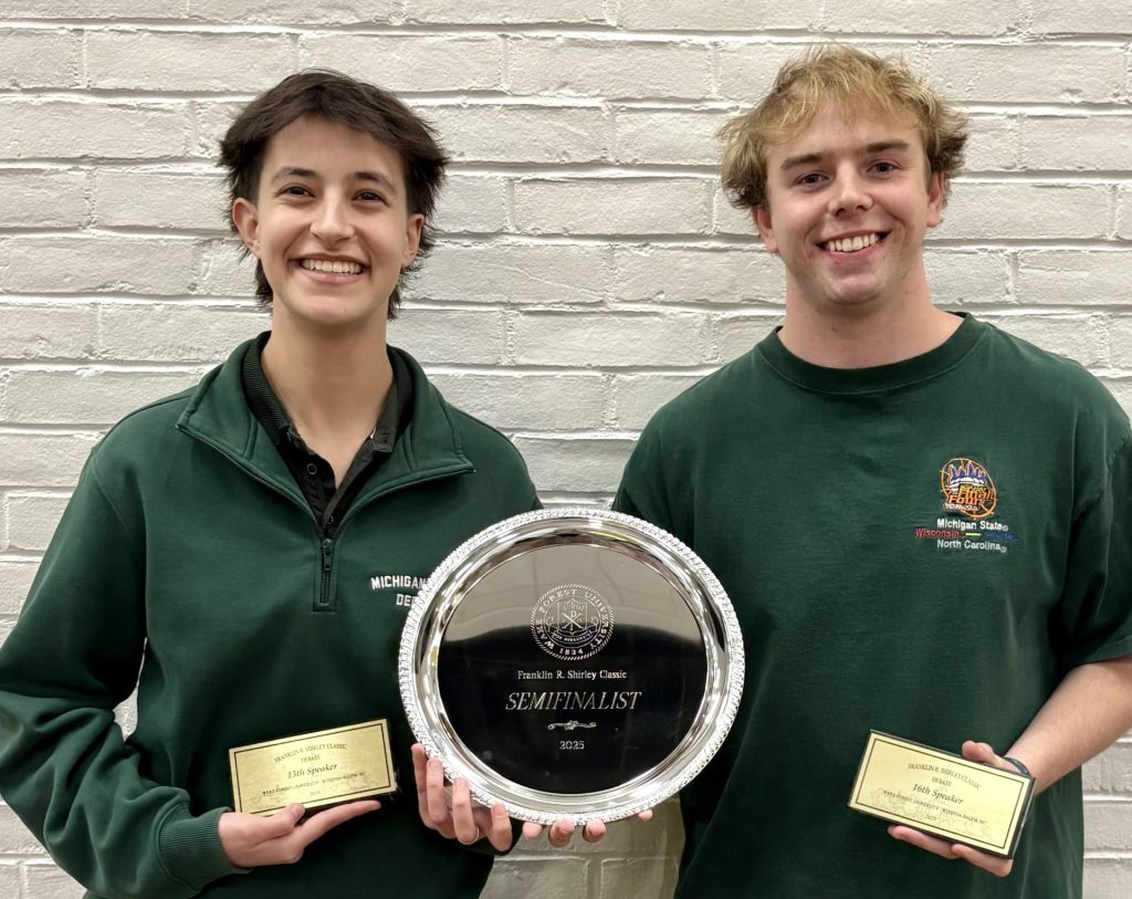 Joanna and Stephen standing in front of a brick wall holding a silver plate award and speaker awards