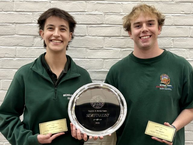 Joanna and Stephen standing in front of a brick wall holding a silver plate award and speaker awards