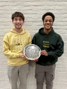 Will and Eleazar standing in front of white brick wall holding silver championship plate