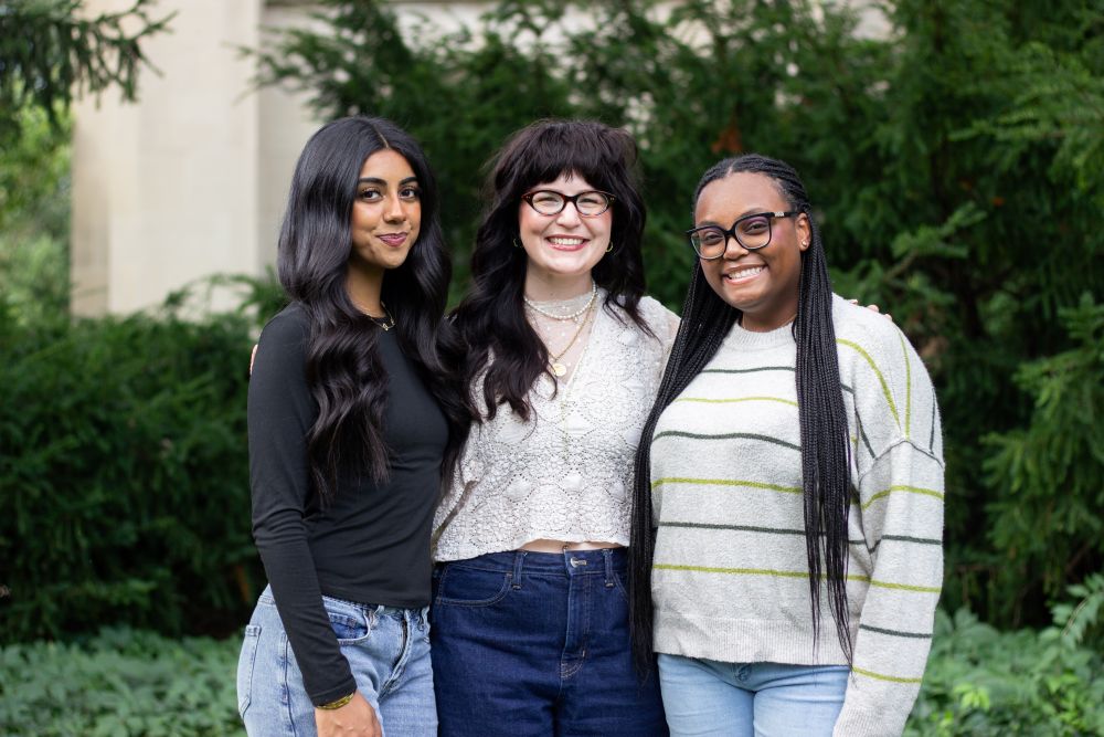 Debater Hina Shehzad (left), Assistant Debate Coach Jasmine Stidham (center), and debater Zaria Jarman (right), standing and smiling in front of greenery at the foot of MSU’s Beaumont Tower. Photo courtesy of Joey Paras, MSU Honors College.